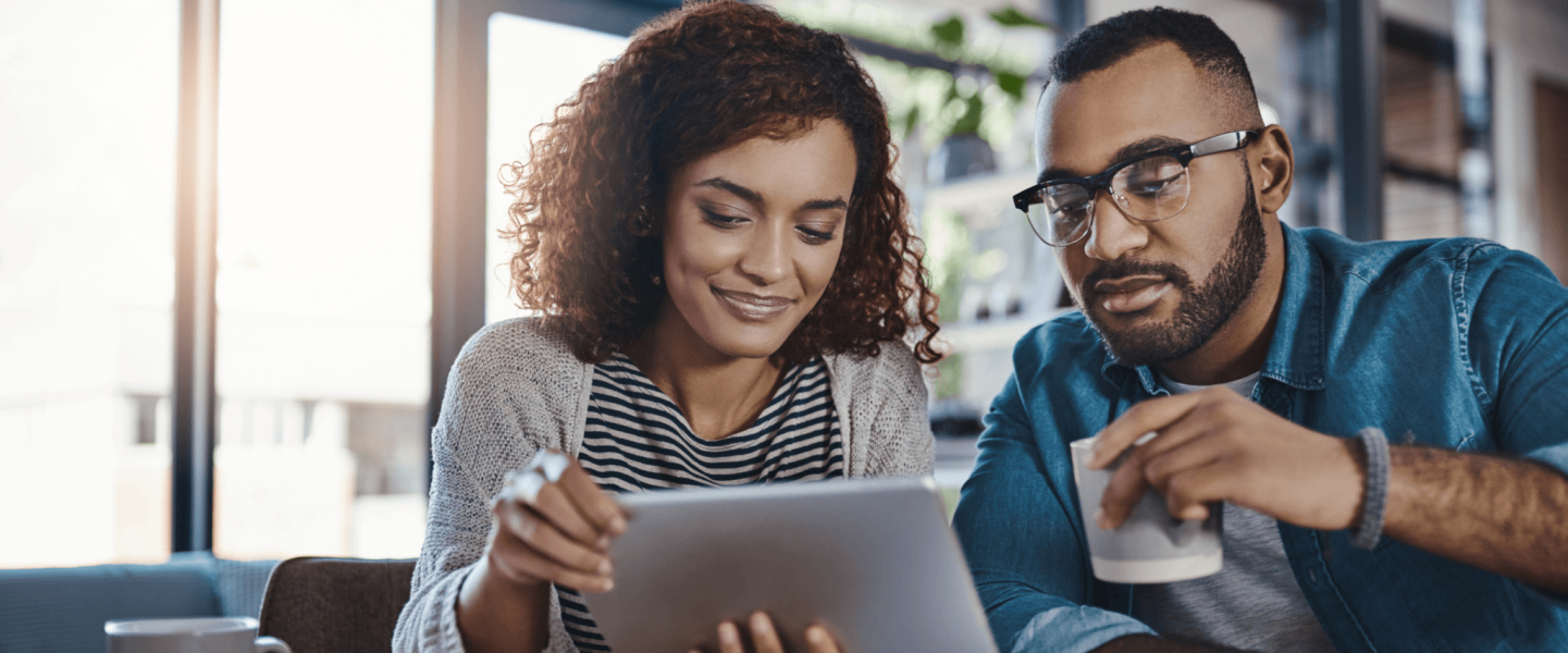 a couple looking at an ipad while drinking coffee
