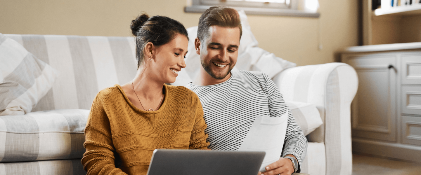 A man and woman sitting on the floor with a laptop and paperwork.