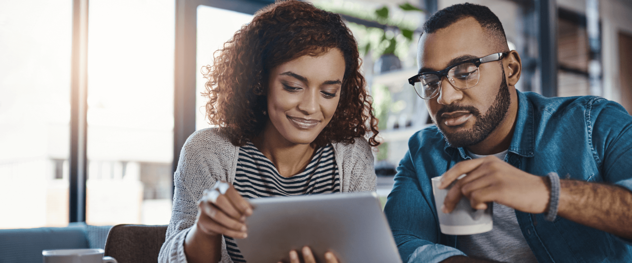 a couple looking at an ipad while drinking coffee
